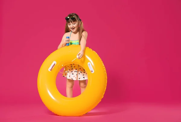 Милая маленькая девочка с надувным кольцом, дующая мыльные пузыри на цветном фоне. — стоковое фото