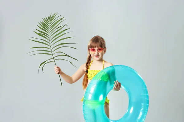 Schattig klein meisje met opblaasbare ring en Palm blad op grijze achtergrond — Stockfoto