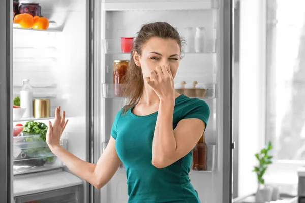 Young woman feeling bad smell from refrigerator in kitchen — Stock Photo, Image