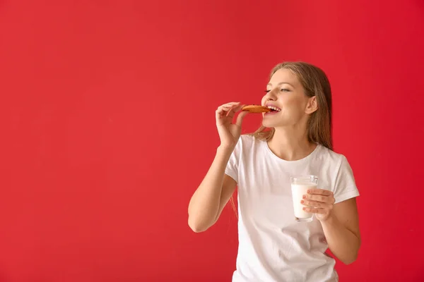 Beautiful young woman with tasty cookie and glass of milk on color background — Stock Photo, Image