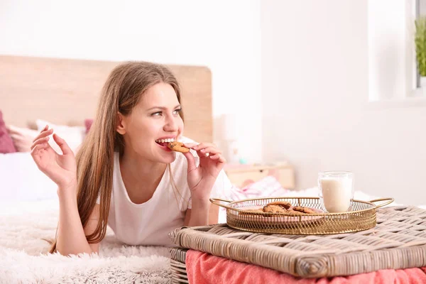 自宅でベッドに横たわっているおいしいクッキーを持つ美しい若い女性 — ストック写真