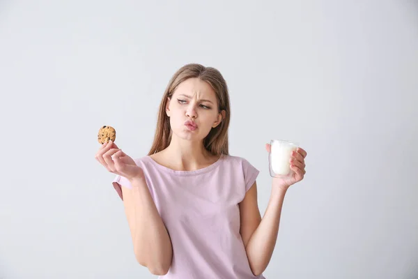 Emotional young woman with tasty cookie and glass of milk on light background — Stock Photo, Image