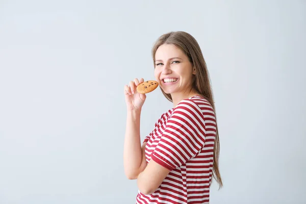 Beautiful young woman with tasty cookie on light background — Stock Photo, Image