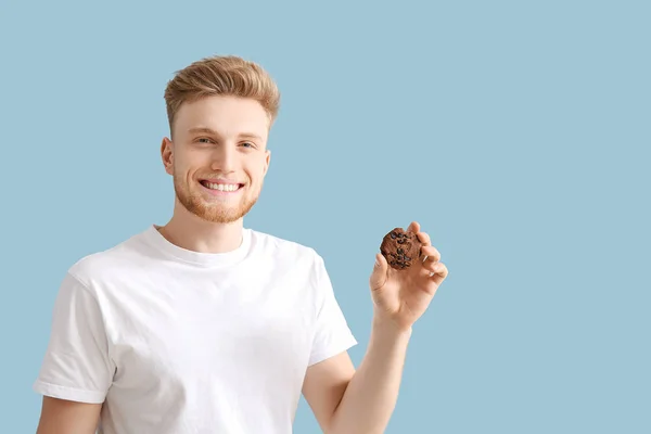 Handsome young man with tasty cookie on color background — Stock Photo, Image