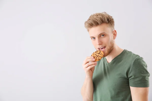 Handsome young man with tasty cookie on light background — Stock Photo, Image