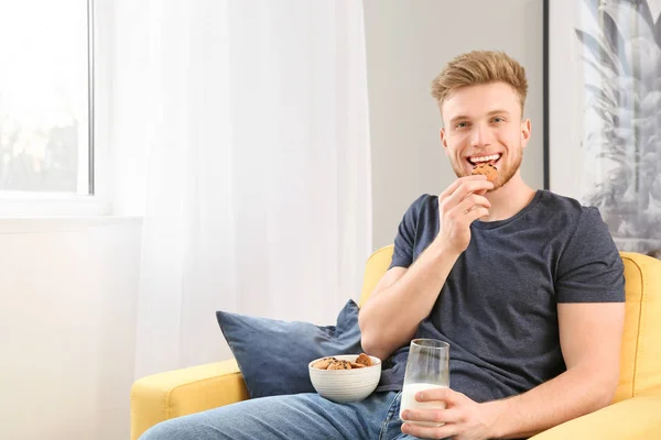 Handsome young man eating tasty cookies with milk at home — Stock Photo, Image