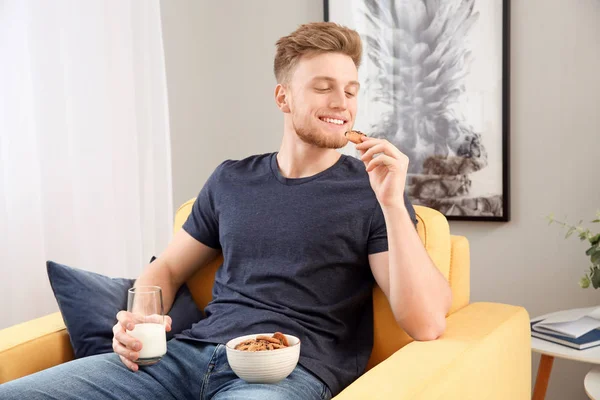 Handsome young man eating tasty cookies with milk at home — Stock Photo, Image