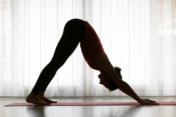 Siluett av sportig ung kvinna praktiserande yoga inomhus — Stockfoto