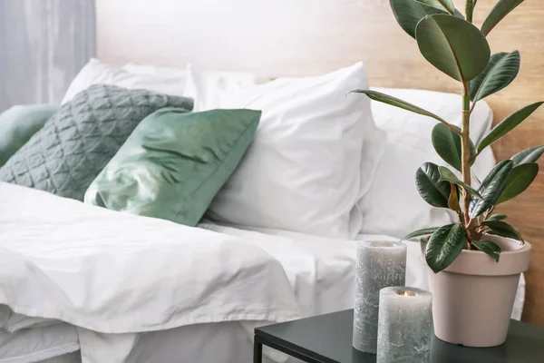 Table with green plants and candles near bed in room — Stock Photo, Image