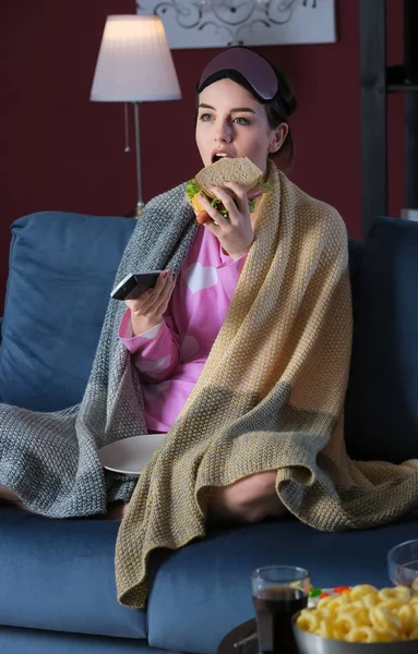 Mooie jonge vrouw eten ongezond eten tijdens het kijken naar TV 's nachts — Stockfoto