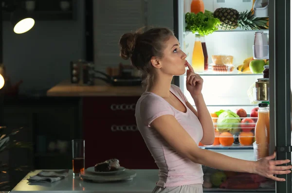 Beautiful young woman looking into fridge at night — Stock Photo, Image