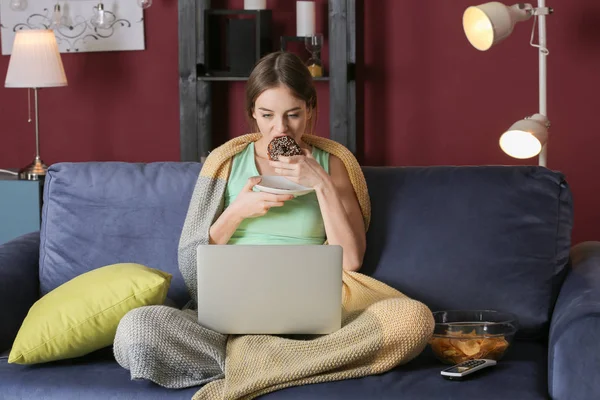 Mooie jonge vrouw met laptop eten ongezond eten 's nachts — Stockfoto
