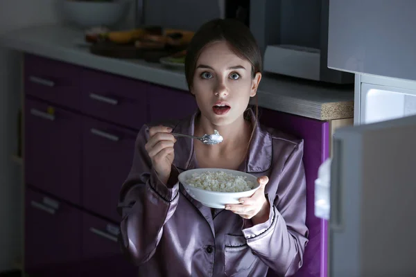 Afraid woman caught in the act of eating tasty food near refrigerator at night — Stock Photo, Image