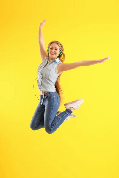 Jumping young woman listening to music on color background — Stock Photo, Image