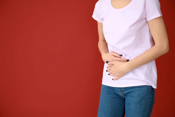 Young woman suffering from abdominal pain on color background — Stock Photo, Image