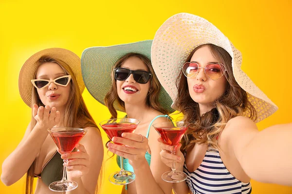 Beautiful young women in swimsuits taking selfie with cocktails on color background — Stock Photo, Image