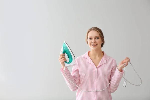 Junge Frau mit Bügeleisen auf hellem Hintergrund — Stockfoto
