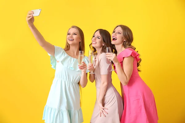 Красивые молодые женщины с бокалами шампанского делают селфи на цветном фоне — стоковое фото