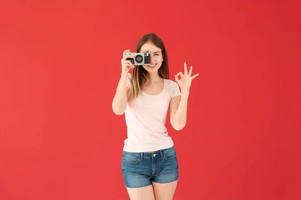 Jonge vrouwelijke fotograaf die OK op kleur achtergrond toont — Stockfoto