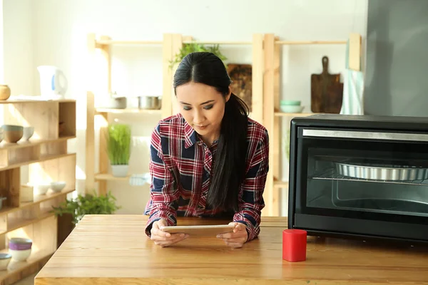 Young Asian woman with tablet PC in kitchen. Modern technology and smart home automation