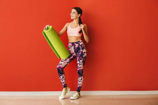 Mujer deportiva con esterilla de yoga cerca de la pared de color — Foto de Stock