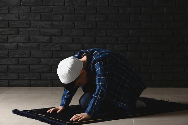 Petit garçon musulman priant contre un mur sombre — Photo