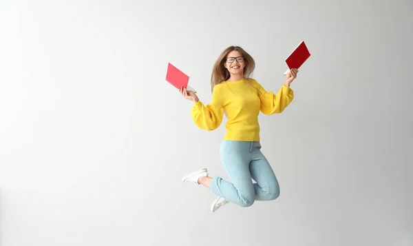Jeune femme sautante avec des livres sur fond clair — Photo