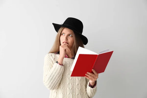 Thoughtful young woman with book on light background — Stock Photo, Image
