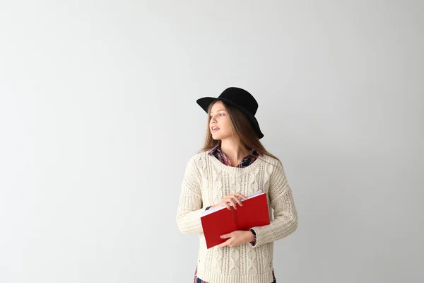 Beautiful young woman with book on light background