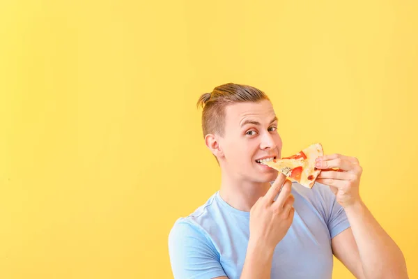 Knappe man eten smakelijke pizza op kleur achtergrond — Stockfoto