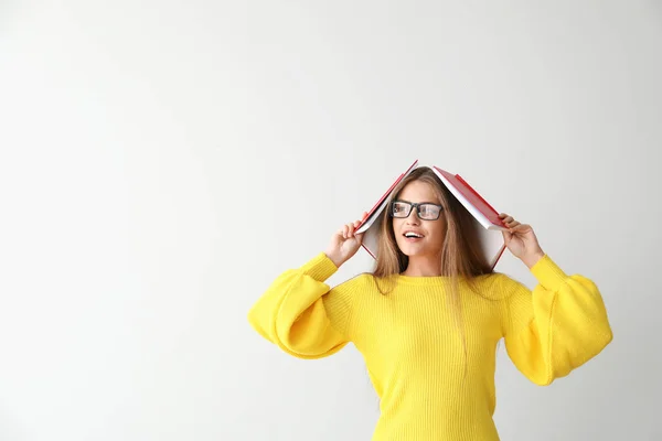 Mujer joven divertida con libros sobre fondo claro — Foto de Stock