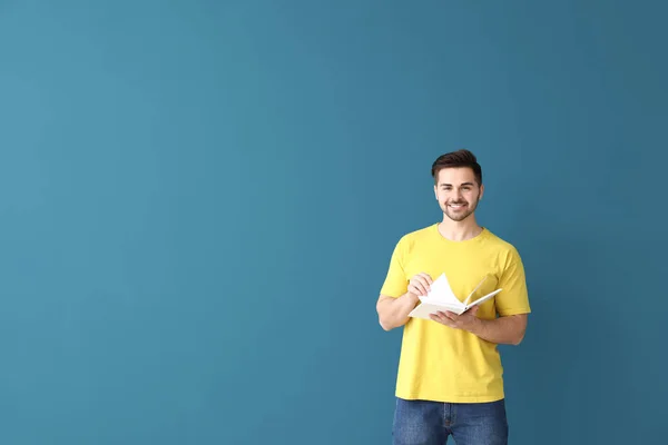 Handsome young man with book on color background — Stock Photo, Image