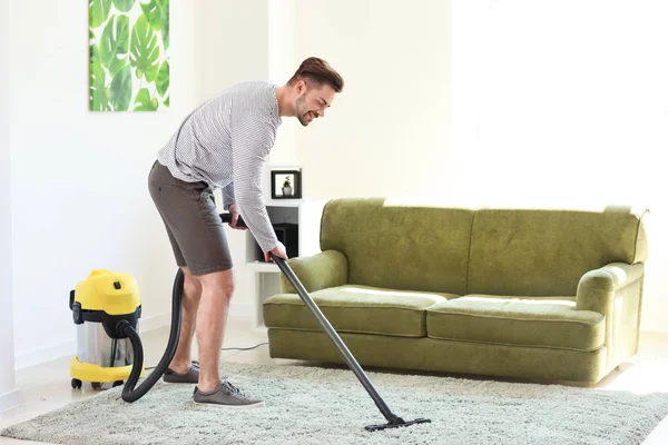 Young man hoovering carpet at home — Stock Photo, Image