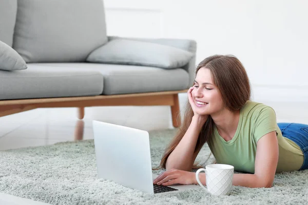 Fiatal nő laptoppal fekvő puha szőnyegen otthon — Stock Fotó