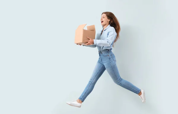 Jumping woman with cardboard box on light background — Stock Photo, Image