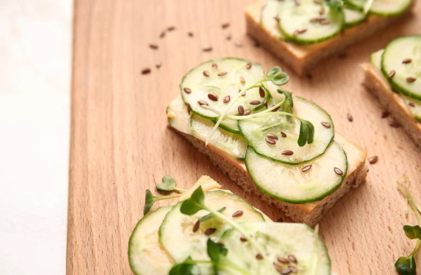 Tasty cucumber sandwiches on wooden board, closeup