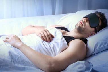 Geceleri yatakta uyuyan maskeli genç adam