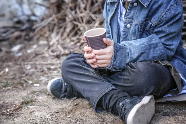 Dakloze jongetje met beker zittend buitenshuis — Stockfoto