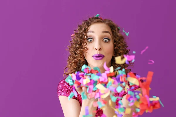 Emotional young woman blowing confetti on color background — Stock Photo, Image