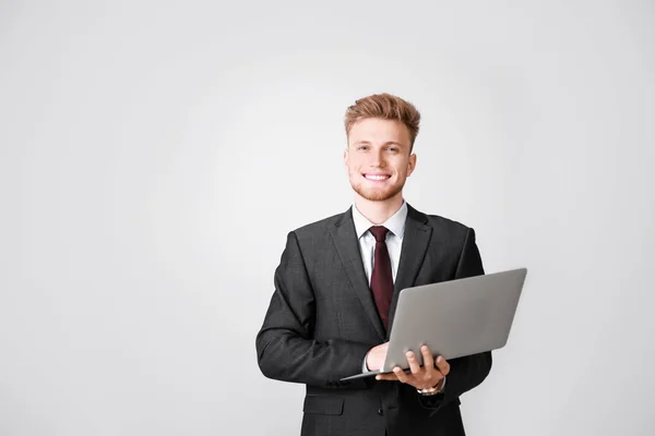 Portrait of businessman with laptop on light background — Stock Photo, Image