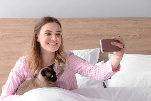Genç kadın yatak odasında sevimli Tay kedisi ile selfie alarak — Stok fotoğraf