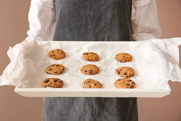 Schöne Bäckerin hält Tablett mit frischen Keksen auf farbigem Hintergrund — Stockfoto
