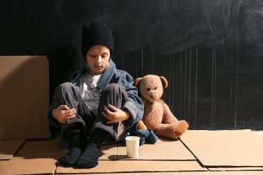 Evsiz küçük kız karanlık duvarın yakınında katta oturan