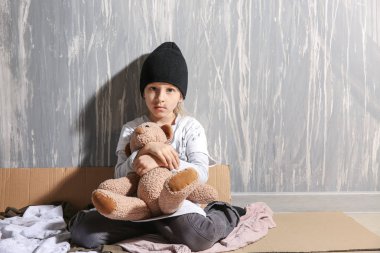 Duvara yakın katta oyuncak ayı ile Evsiz küçük kız