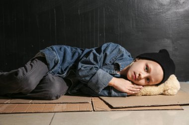 Evsiz küçük kız karanlık duvarın yakınında yerde yatıyor
