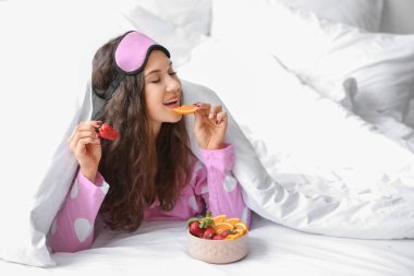 Güzel genç bir kadın yatakta kahvaltı yapıyor.