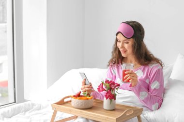 Cep telefonu ile yatakta kahvaltı güzel genç kadın