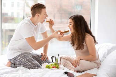 Sevimli genç çift yatakta kahvaltı yapıyor