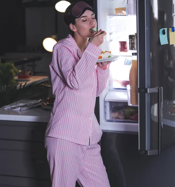 Красива молода жінка їсть їжу біля холодильника вночі — стокове фото