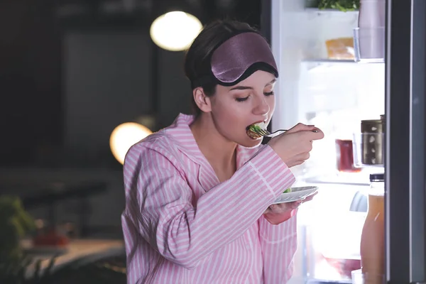Красива молода жінка їсть їжу біля холодильника вночі — стокове фото